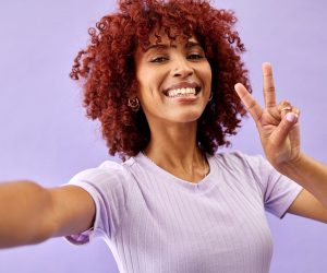Smile, peace sign and portrait of a woman with a selfie on a purple background for fashion. Happy, emoji hand and girl or model with a gesture and taking a photo with a cool attitude for social media