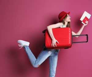 Woman traveler with suitcase on color background